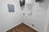 Inviting laundry nook with sleek white walls and warm wooden flooring, featuring convenient wall-mounted storage and modern electrical fittings.