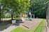 Charming playground nestled in lush greenery with swings, a slide, and climbing structure, perfect for outdoor family fun.