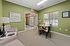 Charming apartment seating area with vibrant green walls, cozy armchairs, and a stylish dining table near sunlit windows.