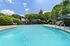 Inviting outdoor pool area with sun loungers and lush greenery, perfect for relaxation under a blue sky.