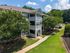 Charming apartment building with white balconies, surrounded by lush greenery and a well-maintained lawn, perfect for relaxed living.