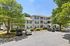 Charming apartment complex with classic architecture, lush greenery, and ample parking under a clear blue sky.