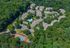 Bird's eye view of a vibrant apartment complex nestled in lush greenery, featuring multiple buildings, a sparkling swimming pool, ample parking, and a colorful tennis court.