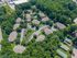 Aerial view of a charming apartment complex surrounded by lush greenery, featuring multiple buildings, ample parking, a swimming pool, and tennis court.
