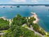 Stunning aerial view of a serene lakeside area with lush greenery, sandy beaches, and secluded islands under a clear blue sky.