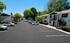 Charming apartment complex surrounded by lush greenery and ample parking space under a sunny blue sky.