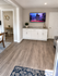 Bright modern living space featuring elegant wood flooring, sleek white cabinetry, and a wall-mounted TV with cityscape visuals.