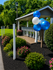 Charming outdoor mail pavilion adorned with vibrant balloons, surrounded by lush greenery and colorful flower beds, offering a welcoming atmosphere.