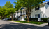 Charming white brick apartment complex with blue accents surrounded by lush green trees and tidy landscaping.