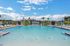 Luxurious apartment complex featuring a pristine swimming pool surrounded by stylish lounge chairs and vibrant palm trees under a stunning blue sky.