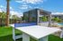 Luxurious outdoor area with modern lounge cabana, ping pong table, palm trees, and sparkling pool under a sunny sky.
