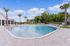 Luxurious outdoor swimming pool area with palm trees, sun loungers, and clear blue skies, perfect for relaxation and leisure in a serene resort-like setting.