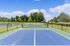 Vibrant outdoor tennis court surrounded by lush greenery, set under a bright blue sky.