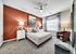 Modern bedroom with a cozy ambiance, featuring a plush bed, stylish accent wall, elegant artwork, and abundant natural light from a large window.