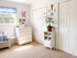Bright and welcoming room with a dresser, decorative plants, and elegant white decor, bathed in natural light.