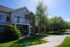 Charming townhouse featuring a welcoming front balcony, surrounded by lush greenery and vibrant landscaping.
