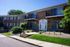 Charming two-story brick apartment complex with private balconies, lush greenery, and a welcoming entrance.