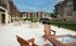 Elegant apartment complex with outdoor patio, cozy seating, modern grills, and lush landscaping under a bright blue sky.