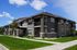 Charming residential apartment building with modern stone and siding exterior, surrounded by lush green lawns and clear blue sky.