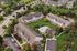 Aerial view of an elegant apartment complex with charming brick facades, lush green lawns, and a central pool area surrounded by trees.
