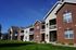 Charming apartment complex with red brick and white siding, featuring inviting balconies and lush green lawns under a clear blue sky.