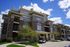 Elegant modern apartment building with spacious balconies, lush landscaping, and a sunny day backdrop.
