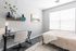 Bright bedroom with a cozy bed, stylish wall art, and a sleek workspace under a large window.
