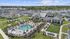 Aerial view of a luxury community featuring modern homes, a stunning pool area, and lush greenery with a scenic pond backdrop.