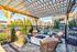 Charming outdoor seating area under a wooden pergola, featuring cozy wicker chairs and a fire pit, with modern apartment buildings in the background.