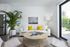 Bright and inviting living room featuring a cozy white sofa with vibrant yellow pillows, complemented by a lush green plant and modern decor. Natural light pours in through a sliding glass door, leading to a serene outdoor space.