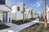 Charming row of modern white townhouses with vibrant purple doors, surrounded by lush landscaping and palm trees under a clear blue sky.