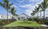Beautiful outdoor community area featuring a modern pavilion surrounded by lush green lawn, tall palm trees, and vibrant landscaping.