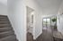 Bright and modern apartment entryway with sleek staircase and dining area leading to a lush garden view.