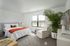 Bright and modern bedroom with plush carpeting, featuring a cozy king-sized bed, stylish armchair, and a large potted plant for a touch of greenery.