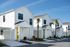 Charming modern townhouses with vibrant colored doors, surrounded by lush landscaping and sunny skies.