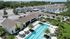Aerial view of a modern housing complex featuring elegant white townhouses, a pristine resort-style swimming pool, and lush landscaping with tall palm trees.