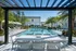 Luxurious apartment complex pool area with stylish cabanas, modern seating, and lush palm trees under a bright blue sky.