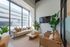 Bright, modern living room with floor-to-ceiling windows, elegant beige sofa, stylish leather chairs, and lush green plants.