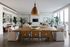 Elegant open-plan living area with modern decor, featuring a large wooden dining table, chic seating, and abundant natural light from floor-to-ceiling windows.