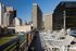 Modern rooftop terrace with chic lounge chairs overlooking a vibrant cityscape and lush green space.