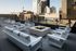 Chic urban rooftop patio with modern white lounge furniture, a central fire pit, and stunning skyline views.