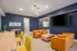 Modern living room with vibrant blue walls, stylish orange chairs, a large wall-mounted TV, and chic wooden furniture creating an inviting atmosphere.