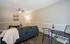 Inviting living room with a modern grey sofa, stylish wall art, and a cozy throw blanket. Features sleek flooring, a chic bar table with wine glasses, and soft lighting for a welcoming ambiance.