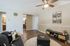 Inviting living room with modern decor, featuring a stylish ceiling fan, artistic wall panels, and a cozy seating area leading to a chic kitchen.