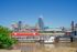 Scenic view of a vibrant cityscape featuring modern skyscrapers, a prominent stadium, and a picturesque waterfront with boats under a clear blue sky.