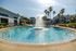 Inviting community pool area with a central water fountain, surrounded by lush palm trees and modern apartment buildings, perfect for relaxing under the sun.