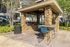 Charming outdoor barbecue area with stone pillars, cozy seating, and lush greenery, perfect for entertaining.