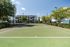 Inviting apartment complex with a lush, landscaped tennis court, offering a serene recreational space under a clear blue sky.