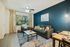 Cozy living room with modern decor featuring a plush gray sofa, vibrant cushions, and a sleek glass-top coffee table. Natural light filters through large windows with patterned curtains, enhancing the serene atmosphere.