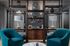 Contemporary living room features elegant wooden shelving, plush teal chairs, and chic lamps, creating a refined and inviting space.
